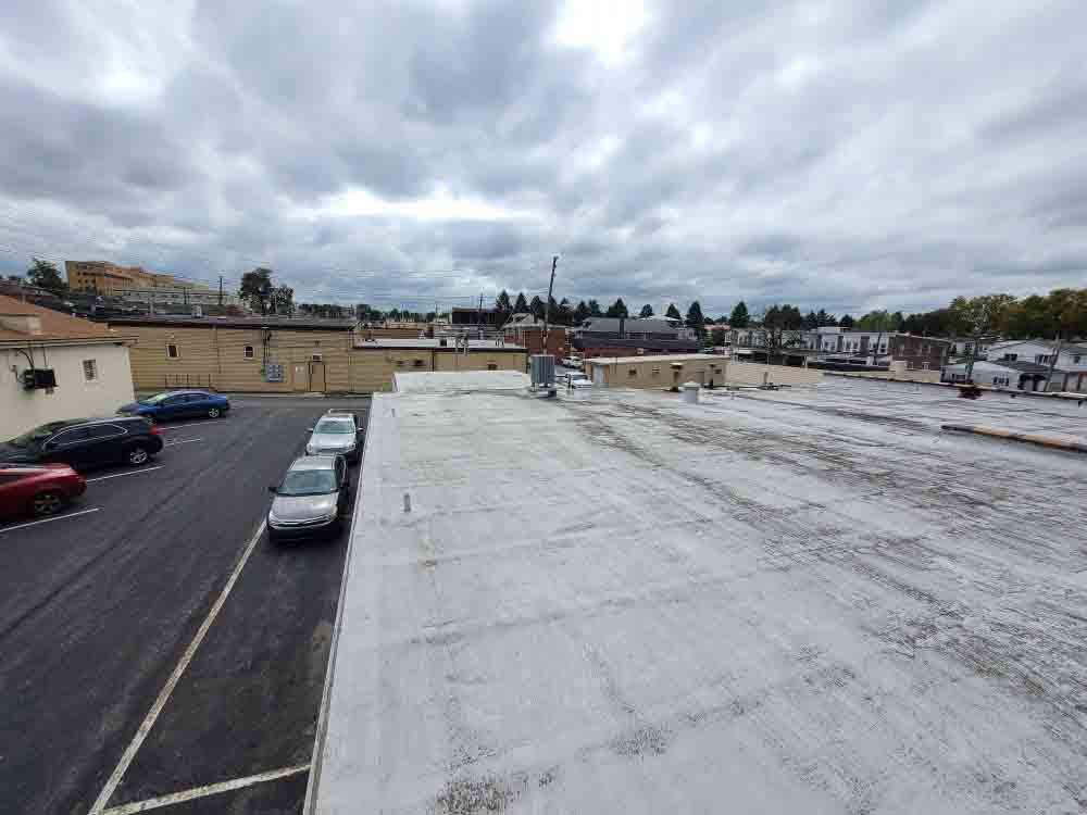 Rooftop parking lot with parked cars under a cloudy sky, showing a wide, mostly empty white roof surface