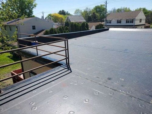 Flat black rooftop with metal railing and neighboring houses under a sunny sky