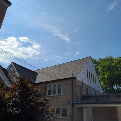 Two-story house with gray roof and light brick walls under a bright blue sky with clouds