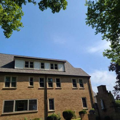 Brick townhouse under blue sky, framed by leafy trees