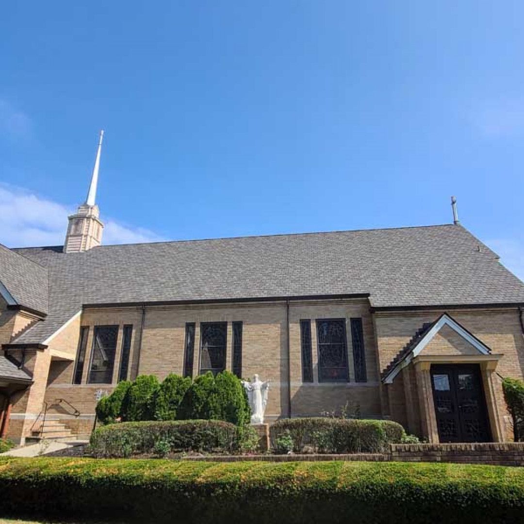 Brick church building with gray roof and tall steeple under a clear blue sky