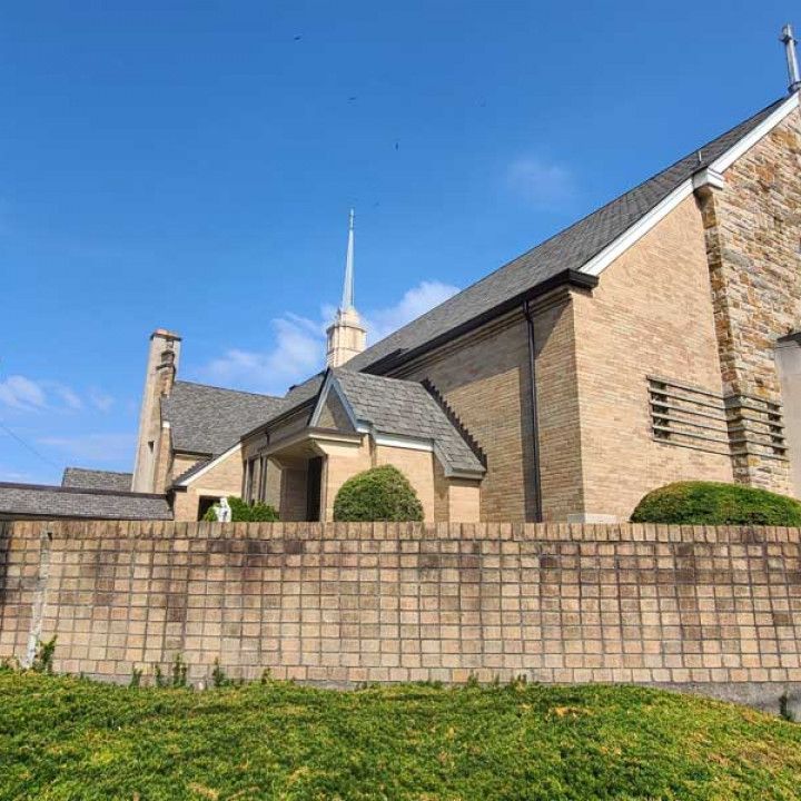 Stone church building with spire behind a low brick wall under a clear blue sky