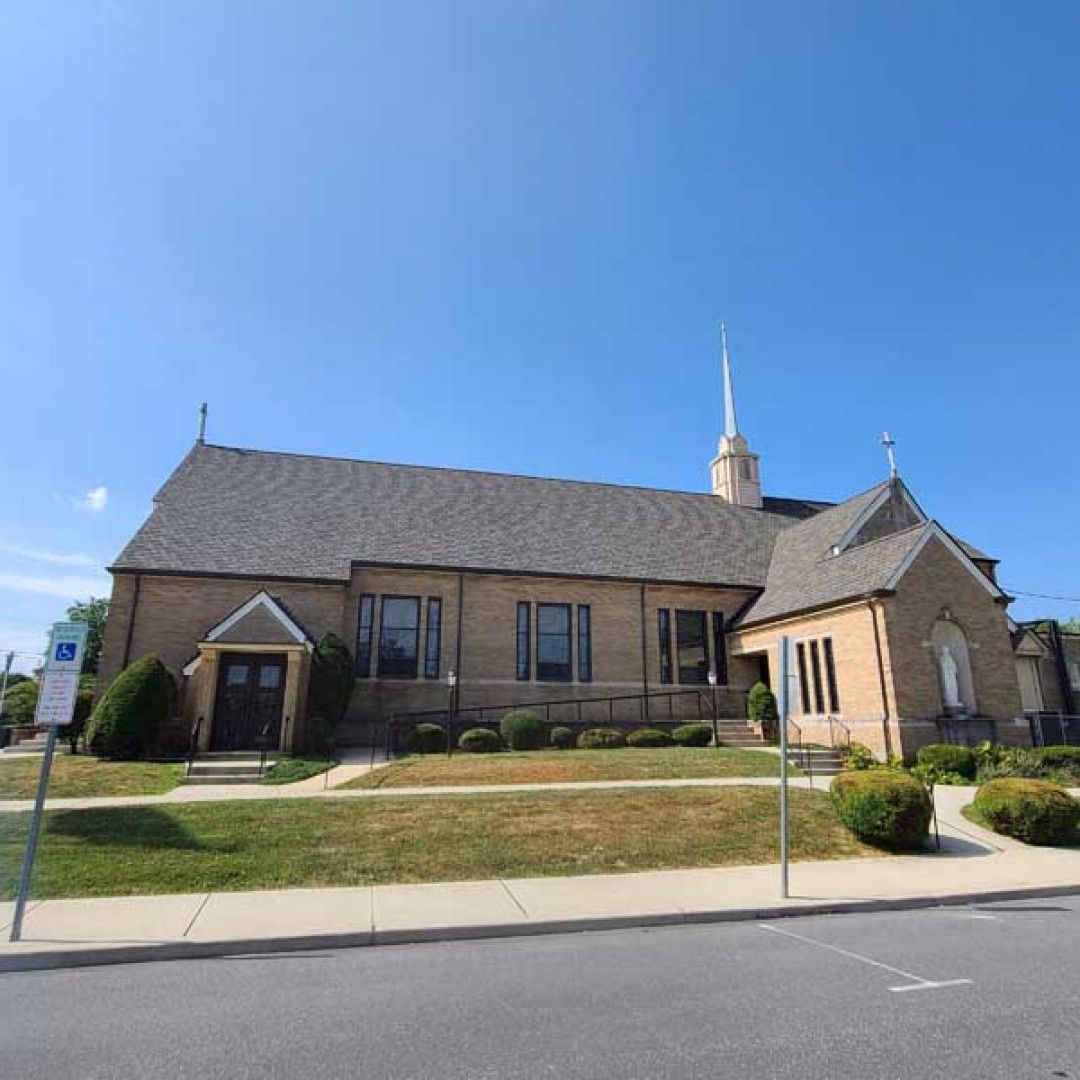 Brick church building with steeple on a sunny street under a clear blue sky