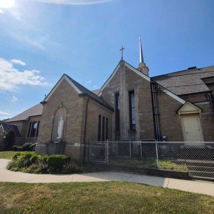 Brick church with a cross and tall steeple behind a chain-link fence on a sunny day