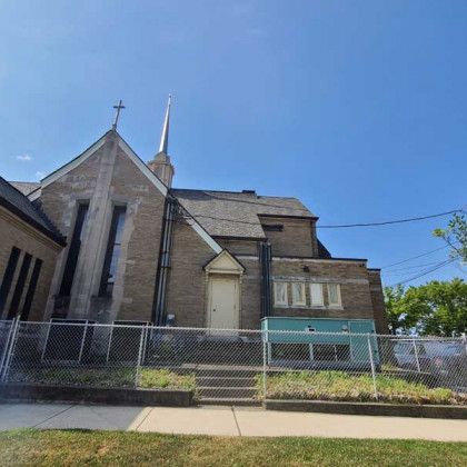 Stone church with a tall steeple behind a chain-link fence under a bright blue sky