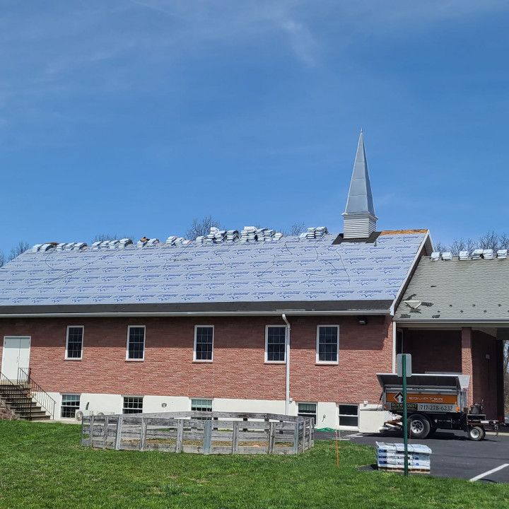 Brick building with a partially shingled roof, small steeple, and a parked utility truck beside it.