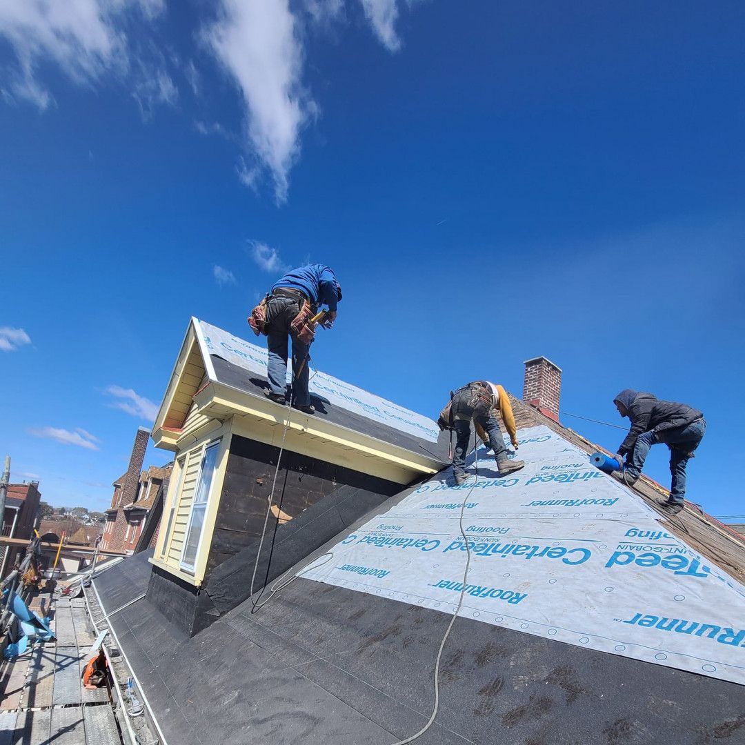 Roofers working on a steep roof under a bright blue sky, installing shingles and flashing