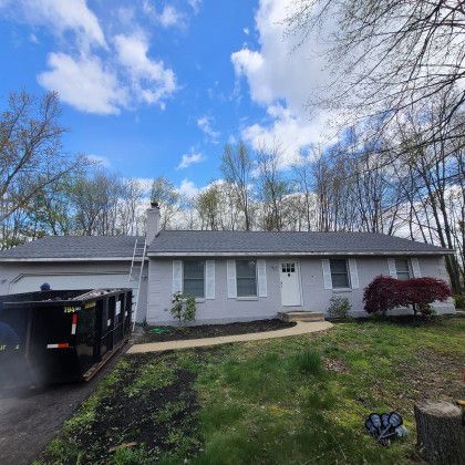 Single-story gray house with a carport, front yard, and blue sky with clouds