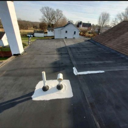 Flat rooftop with black membrane, white vents, and a white house in the background