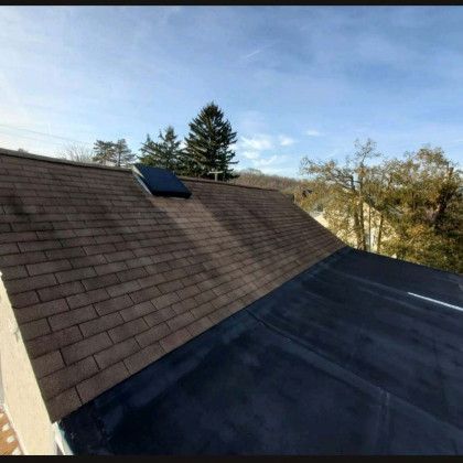 House roof with dark shingles and a small solar panel under a clear sky