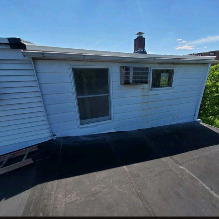 Rooftop deck with black surface beside a white house exterior and sliding glass door under a blue sky