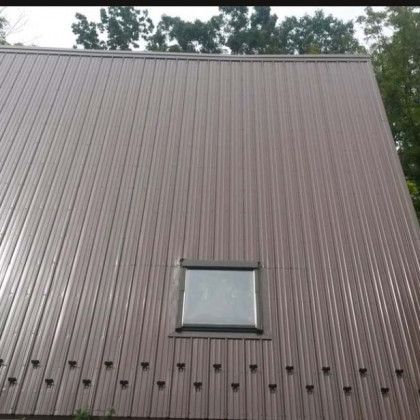 Brown corrugated metal wall with a small square window and trees visible above the roofline