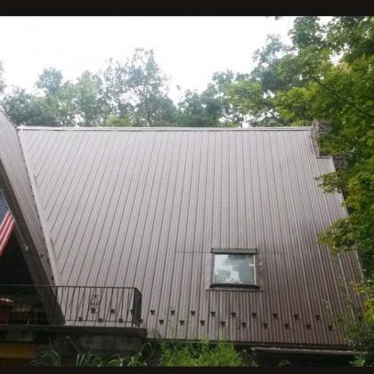 A brown house wall with a small window, surrounded by trees and viewed from below.