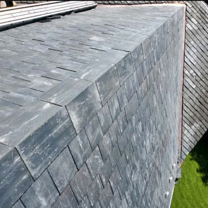 Gray slate shingle roof with steep intersecting slopes above a green lawn