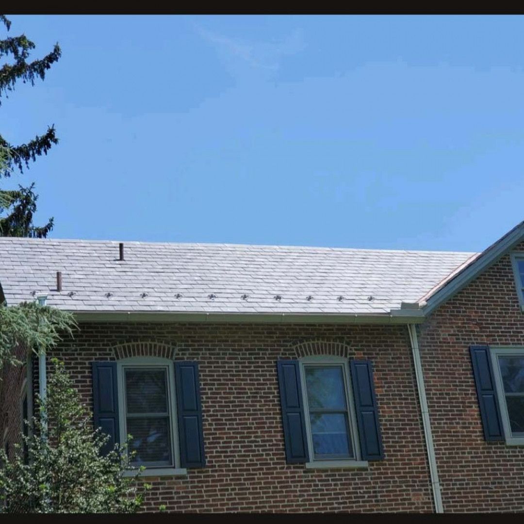 Brick house roof with gray shingles and blue shutters under a clear blue sky