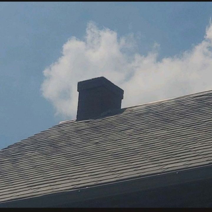 Roof with gray shingles and a black chimney against a blue sky with a white cloud
