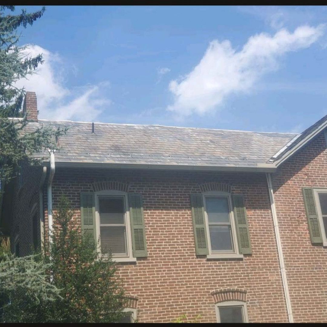 Brick house with gray shutters and a sloped roof under a blue sky with clouds