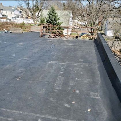Flat black rooftop with a low parapet, trees and houses visible in the background.