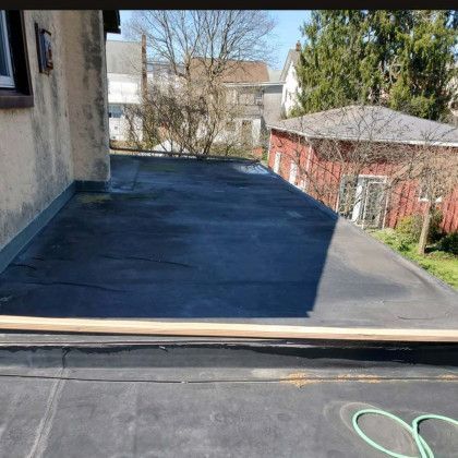 Backyard patio with dark roofing, house wall on left, red shed and trees in the background