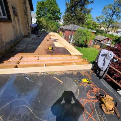 Roofer installing plywood on a flat roof, with tools and orange extension cords in bright sunlight.
