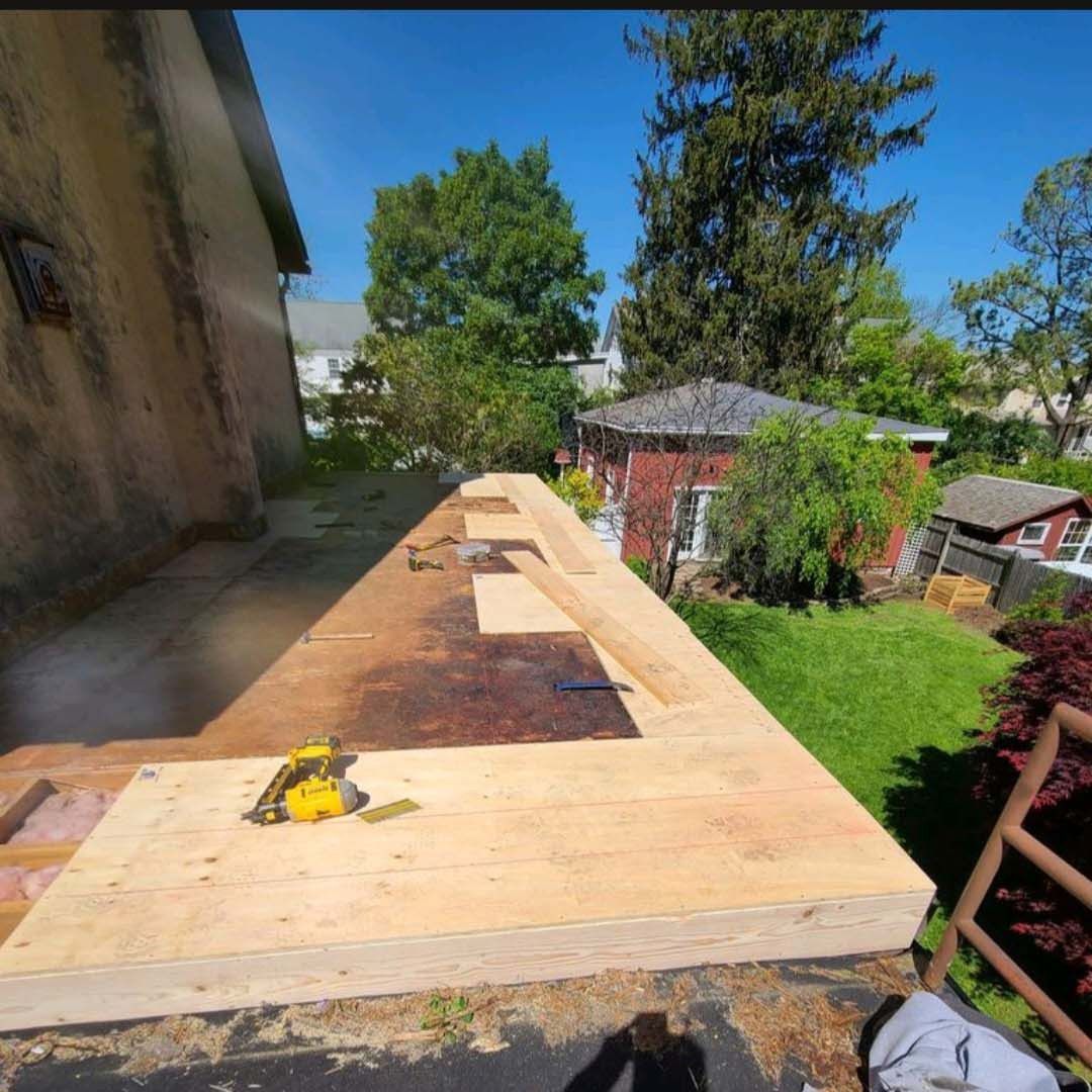Outdoor concrete slab next to a house, with a small yellow flower and a yard with trees and a gazebo.