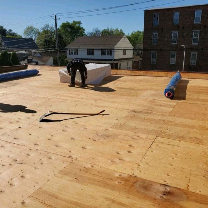 Roofing workers installing white material on a flat roof on a sunny day, with rolled roofing nearby