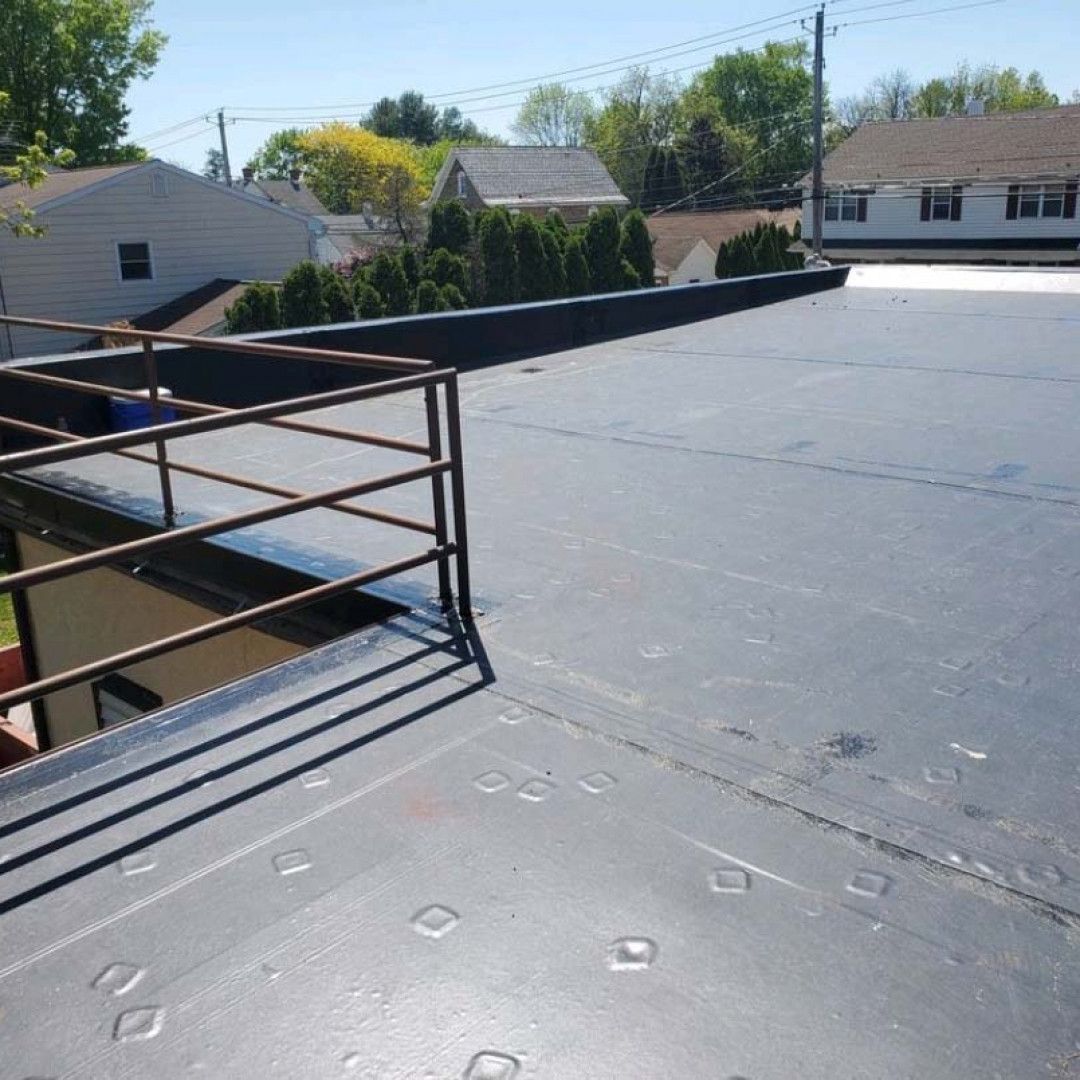 Flat rooftop with white membrane, metal railing, and houses and trees in the background