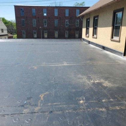 Flat black rooftop beside a beige building, with a brick building in the background.