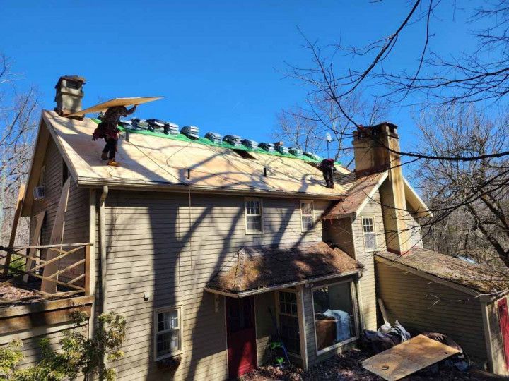 Roofers repairing a beige house roof with green tarp under a clear blue sky