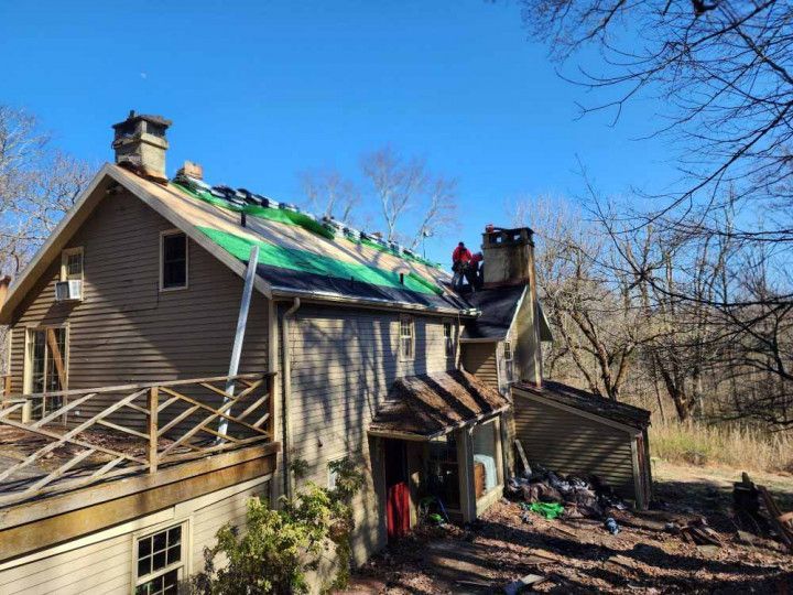Damaged house with a collapsed roof and fire damage, debris outside under a clear blue sky
