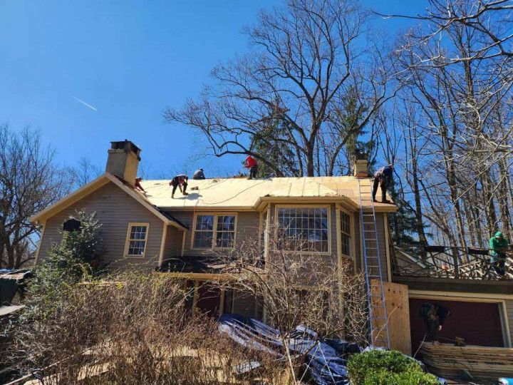 House roof with workers repairing shingles under a clear blue sky
