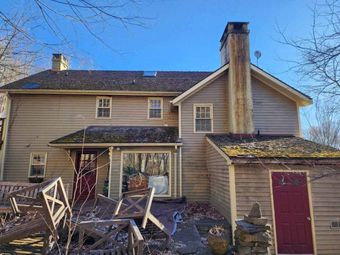 Damaged two-story house with broken porch and scattered debris in front yard