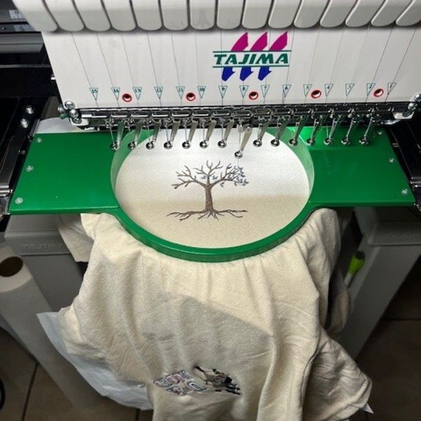 An embroidery machine stitching a tree design onto a light-colored fabric.