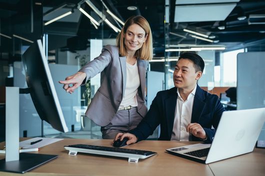 Two smiling employees working together are focused on a computer