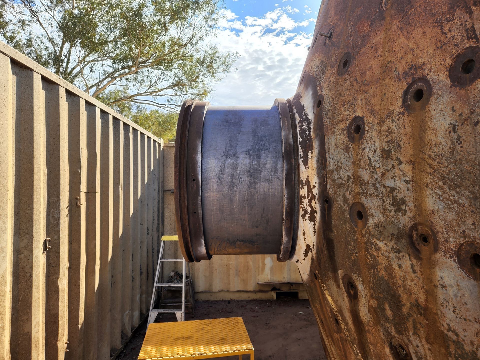 A ladder is sitting next to a large rusty metal object.