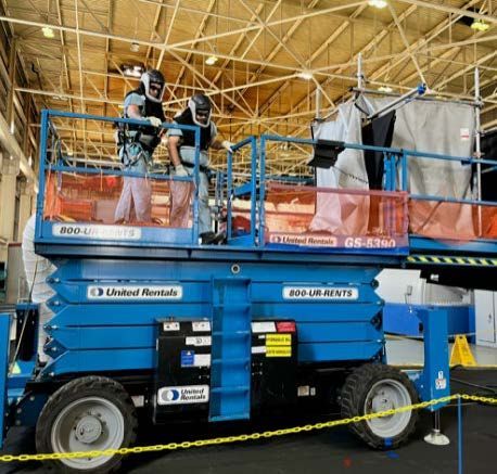 A blue united rentals scissor lift with two people on it