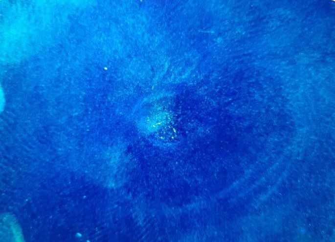 A close up of a blue water surface with bubbles coming out of it.