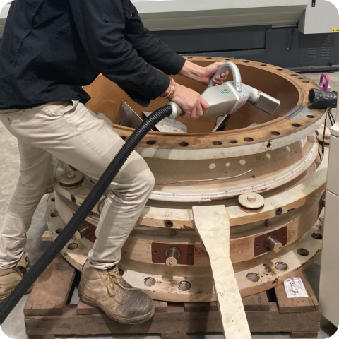 A man is using a vacuum cleaner to clean a large piece of metal