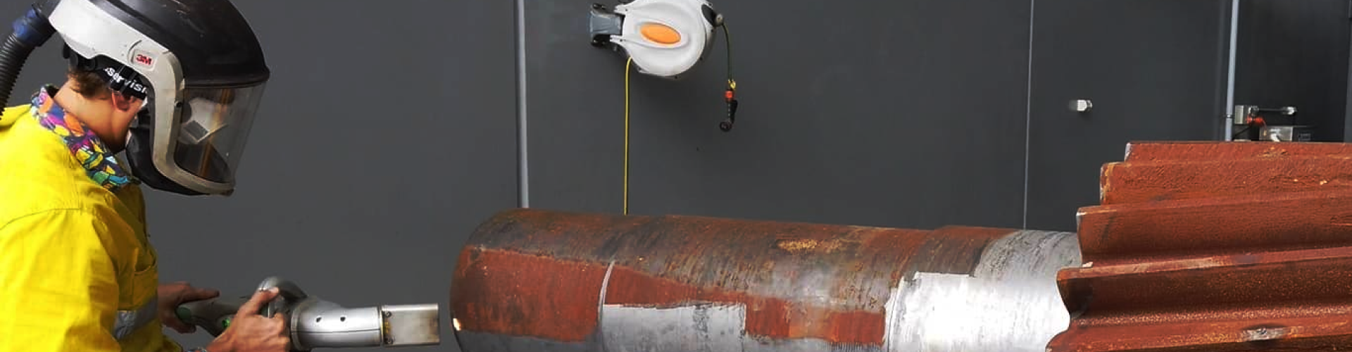 A man wearing a welding helmet is working on a large piece of metal.