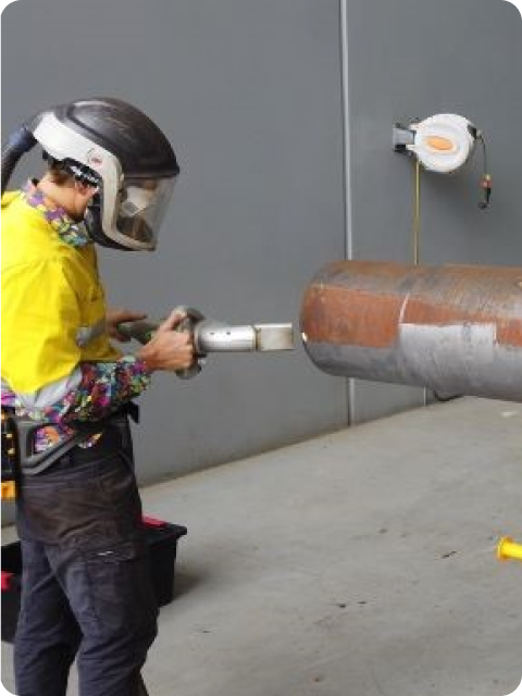 A man wearing a welding helmet is working on a pipe