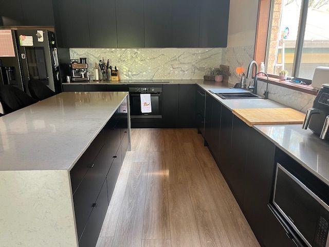 A dark kitchen area with grey stone kitchen island— Tefa Kitchens & Joinery in Cessnock, NSW