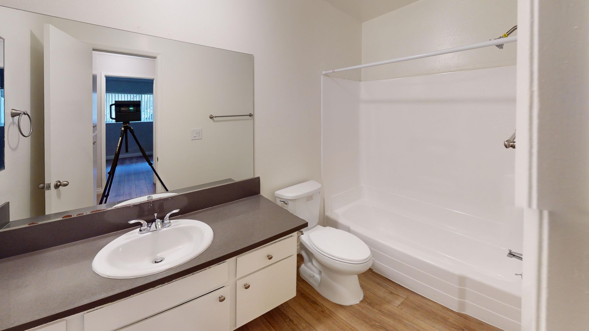 Bathroom with a sink, toilet, and bathtub/shower. Neutral tones, a large mirror, and open door.