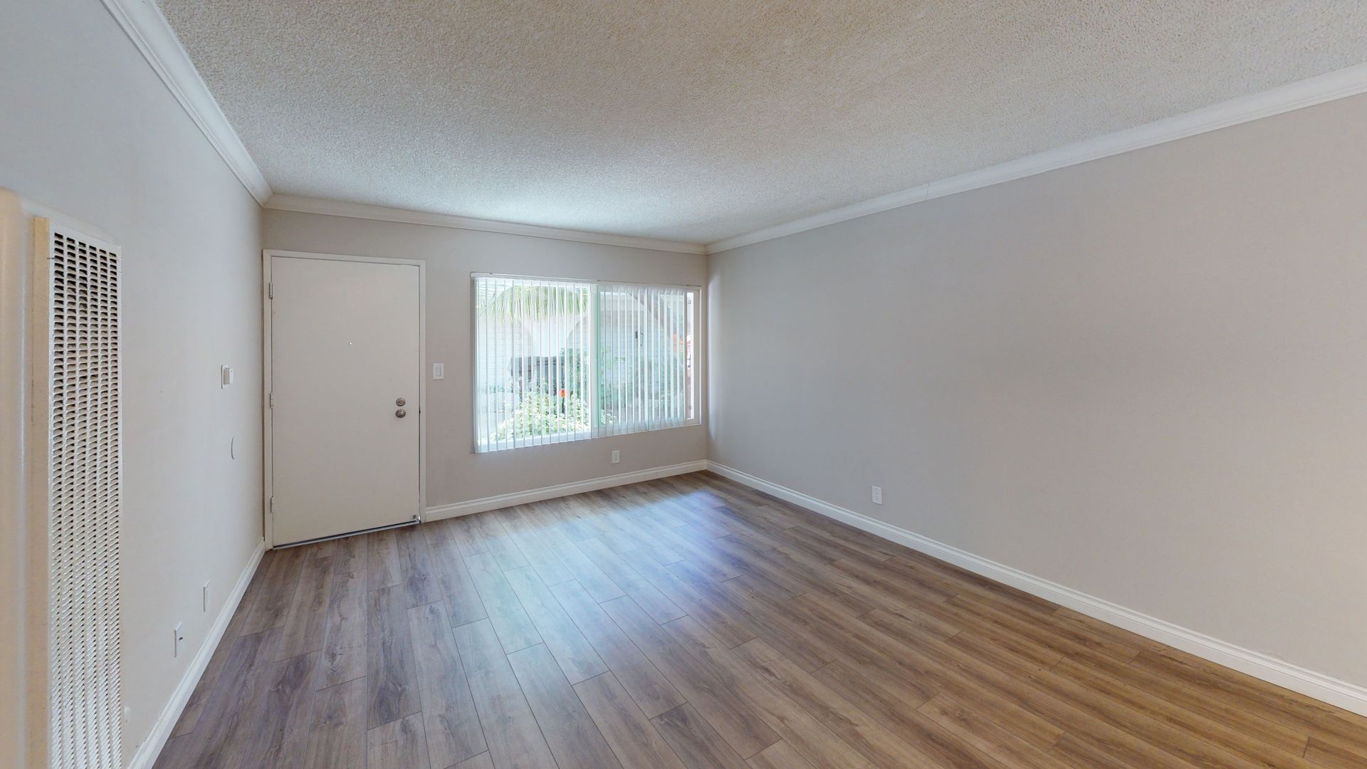 Empty room with a window and a door, featuring wood-look flooring and beige walls.