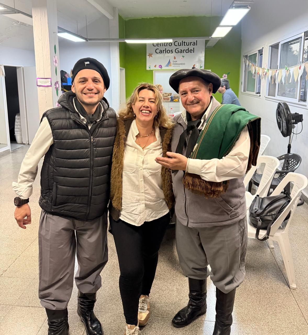 Tres personas sonriendo en un espacio interior, una de ellas vestida de gaucho.