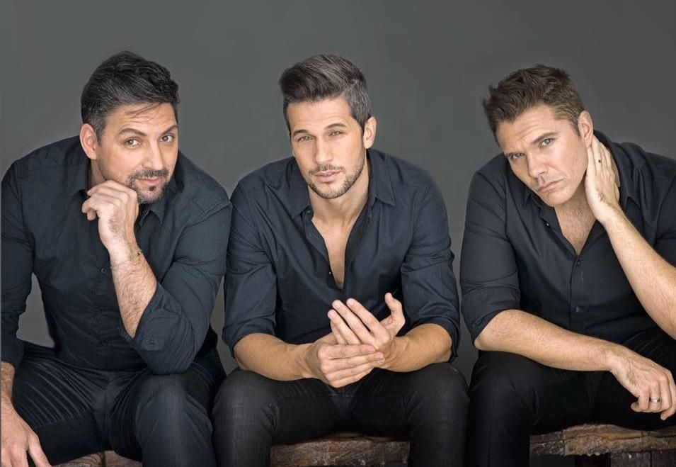 Tres hombres con camisas negras sentados juntos, mirando hacia la cámara.