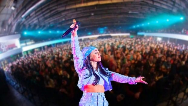 Cantante actuando en el escenario, levantando los brazos hacia una gran multitud, vistiendo un traje azul.
