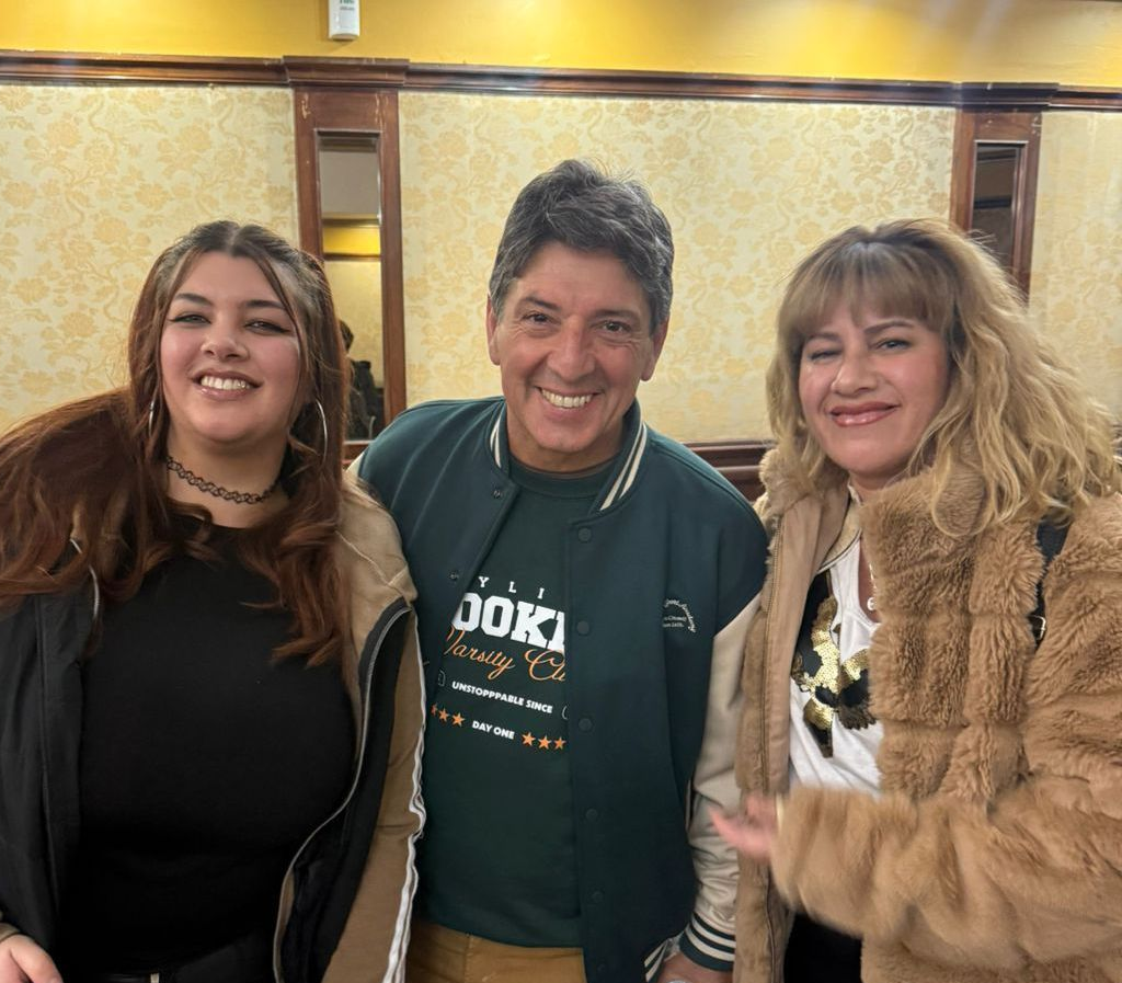 Tres personas sonriendo y posando en una habitación con una pared estampada.