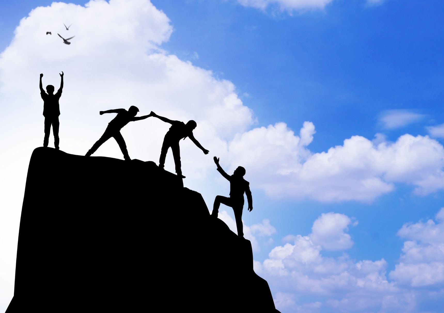A group of people helping each other climb a mountain
