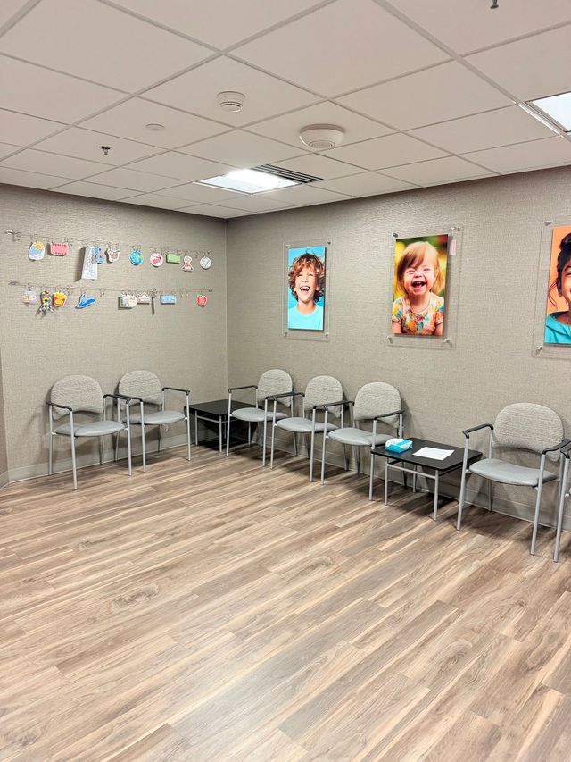 Empty waiting room with gray walls, wood floor, chairs, and colorful portrait art on the wall.