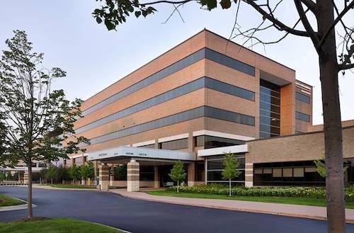 Modern office building with orange brick and dark windows beside a road and trees